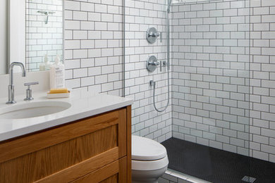 Inspiration for a mid-sized modern bathroom in Portland with recessed-panel cabinets, medium wood cabinets, a one-piece toilet, white tile, ceramic tile, white walls, ceramic floors, an undermount sink, engineered quartz benchtops, black floor, a hinged shower door and white benchtops.