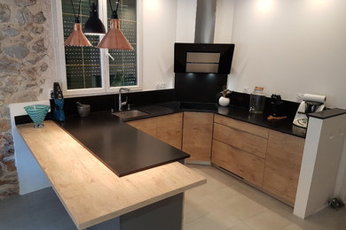 Exemple d'une cuisine ouverte moderne en U et bois clair avec un évier 1 bac, une crédence noire, un électroménager de couleur, un sol en carrelage de porcelaine, une péninsule, un sol beige et plan de travail noir.