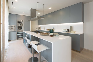 Contemporary kitchen in London with flat-panel cabinets, grey cabinets, white splashback, stainless steel appliances, light hardwood floors, with island, beige floor and white benchtop.