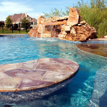Free form pool with stone table, sun shelf, water feature, and outdoor kitchen,