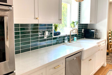 Example of a transitional galley kitchen design with a farmhouse sink, shaker cabinets, white cabinets, quartz countertops, green backsplash, granite backsplash and stainless steel appliances