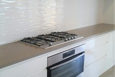 Photo of a modern galley kitchen in Newcastle - Maitland with a double-bowl sink, white cabinets, quartzite benchtops, white splashback, stainless steel appliances, with island and beige floor.