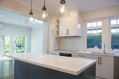 Inspiration for a mid-sized traditional galley open plan kitchen in Melbourne with a drop-in sink, shaker cabinets, white cabinets, quartz benchtops, white splashback, subway tile splashback, black appliances, dark hardwood floors and with island.