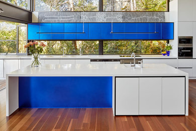 Photo of a large modern l-shaped open plan kitchen in Sydney with a double-bowl sink, flat-panel cabinets, blue cabinets, solid surface benchtops, panelled appliances, medium hardwood floors, with island and brown floor.