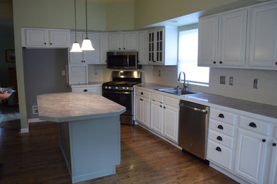 Mid-sized traditional l-shaped kitchen in Denver with raised-panel cabinets, white cabinets, laminate benchtops, grey splashback, porcelain splashback, stainless steel appliances and with island.