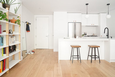Example of a small trendy single-wall light wood floor and brown floor open concept kitchen design in New York with a drop-in sink, flat-panel cabinets, white cabinets, quartzite countertops, white backsplash, mosaic tile backsplash, stainless steel appliances, an island and white countertops