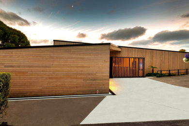 This is an example of a mid-sized contemporary two-storey brown house exterior in Christchurch with wood siding, a flat roof, a metal roof and a black roof.