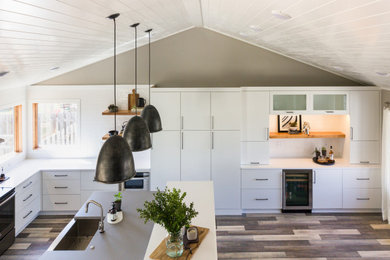 Open concept kitchen - large industrial l-shaped light wood floor and multicolored floor open concept kitchen idea in Other with an undermount sink, white cabinets, quartz countertops, stainless steel appliances, an island and white countertops