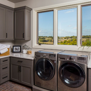オースティンの中サイズのトラディショナルスタイルのおしゃれな洗濯室 (シェーカースタイル扉のキャビネット、グレーのキャビネット、人工大理石カウンター、グレーの壁、レンガの床、左右配置の洗濯機・乾燥機、茶色い床) の写真