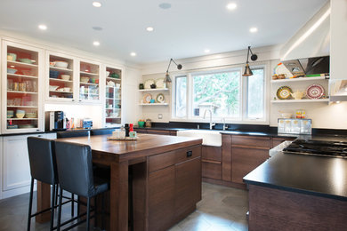 Enclosed kitchen - contemporary u-shaped porcelain tile enclosed kitchen idea in Ottawa with a farmhouse sink, flat-panel cabinets, medium tone wood cabinets, granite countertops, black backsplash, paneled appliances and an island