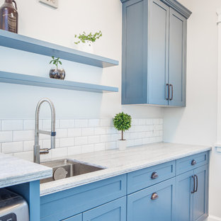 Diseño de lavadero multiusos y de galera, de estilo de casa de campo, pequeño, con fregadero bajoencimera, armarios estilo shaker, puertas de armario azules, encimera de acrílico, paredes grises, suelo de baldosas de porcelana, lavadora y secadora juntas, suelo gris y encimeras grises