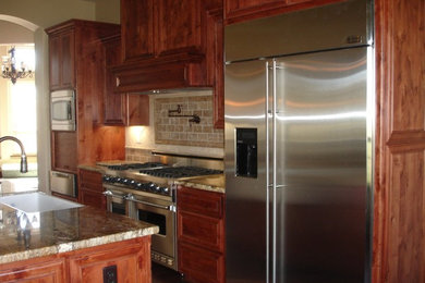 Example of a tuscan open concept kitchen design in Sacramento with a farmhouse sink, raised-panel cabinets, granite countertops, beige backsplash, stone tile backsplash and stainless steel appliances