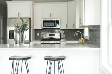Open concept kitchen - mid-sized transitional u-shaped dark wood floor and brown floor open concept kitchen idea in New York with a farmhouse sink, shaker cabinets, white cabinets, quartz countertops, gray backsplash, glass tile backsplash, stainless steel appliances and a peninsula