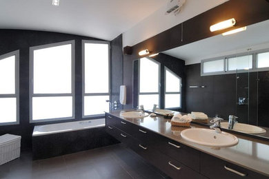 Large minimalist master black tile porcelain tile and black floor drop-in bathtub photo in Los Angeles with flat-panel cabinets, black cabinets, black walls, a drop-in sink and beige countertops