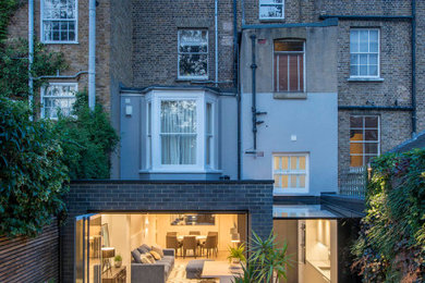 Photo of a large contemporary rear house exterior in London with four floors, mixed cladding and a butterfly roof.
