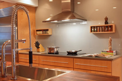 Inspiration for a contemporary galley eat-in kitchen remodel in San Francisco with an undermount sink, flat-panel cabinets, light wood cabinets, limestone countertops, gray backsplash, glass sheet backsplash and stainless steel appliances