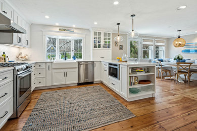 Mid-sized beach style u-shaped medium tone wood floor and brown floor eat-in kitchen photo in Boston with a farmhouse sink, shaker cabinets, white cabinets, quartz countertops, white backsplash, ceramic backsplash, stainless steel appliances, a peninsula and white countertops