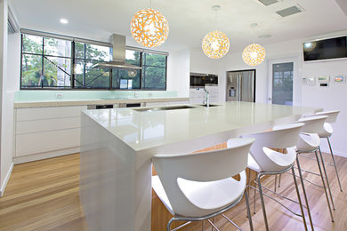 Expansive modern galley separate kitchen in Brisbane with an undermount sink, white cabinets, granite benchtops, stainless steel appliances, light hardwood floors, with island and white benchtop.