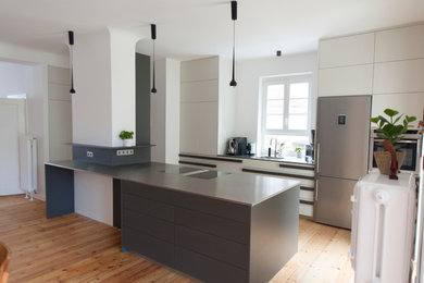 Photo of a large contemporary galley eat-in kitchen in Berlin with an integrated sink, flat-panel cabinets, grey cabinets, stainless steel benchtops, white splashback, stainless steel appliances and with island.