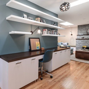 Imagen de despacho tradicional renovado, de tamaño medio, con paredes azules, suelo de madera clara, chimenea tradicional, marco de chimenea de piedra, escritorio empotrado y suelo marrón