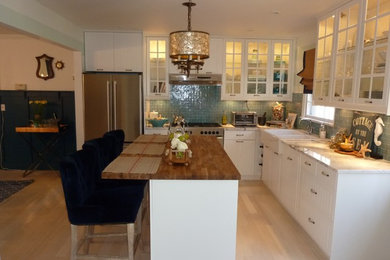 Inspiration for a mid-sized coastal l-shaped light wood floor and beige floor eat-in kitchen remodel in New York with a farmhouse sink, glass-front cabinets, white cabinets, granite countertops, blue backsplash, mosaic tile backsplash, stainless steel appliances and an island