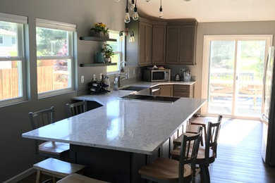Transitional galley medium tone wood floor and brown floor eat-in kitchen photo in Cleveland with a farmhouse sink, shaker cabinets, medium tone wood cabinets, stainless steel appliances, a peninsula and gray countertops