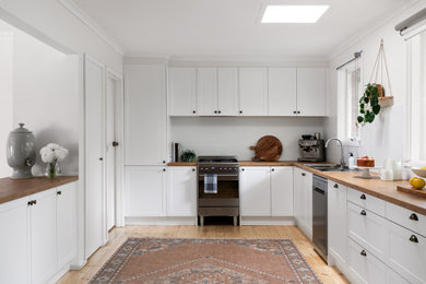 Photo of a large scandinavian u-shaped kitchen pantry in Melbourne with a drop-in sink, shaker cabinets, white cabinets, laminate benchtops, white splashback, subway tile splashback, stainless steel appliances and light hardwood floors.