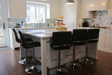 Example of a mid-sized transitional u-shaped medium tone wood floor open concept kitchen design in New York with a drop-in sink, shaker cabinets, white cabinets, marble countertops, multicolored backsplash, glass tile backsplash, stainless steel appliances and an island
