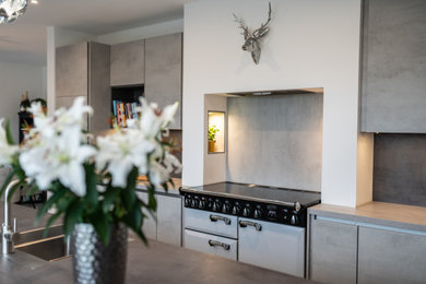 This is an example of a large contemporary single-wall open plan kitchen in Other with a built-in sink, flat-panel cabinets, grey cabinets, laminate countertops, grey splashback, stainless steel appliances, an island, grey worktops and feature lighting.