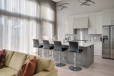Example of a transitional light wood floor kitchen design in Calgary with an undermount sink, shaker cabinets, white cabinets, quartzite countertops, gray backsplash, ceramic backsplash, stainless steel appliances and an island