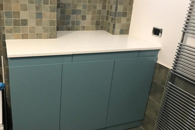 Foto di una piccola lavanderia multiuso moderna con ante lisce, ante blu, top in legno, pareti multicolore, pavimento con piastrelle in ceramica, lavatrice e asciugatrice nascoste, pavimento multicolore e top bianco