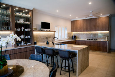 This is an example of an expansive modern u-shaped eat-in kitchen in Sydney with a double-bowl sink, flat-panel cabinets, brown cabinets, tile benchtops, beige splashback, porcelain splashback, black appliances, porcelain floors, a peninsula, beige floor and beige benchtop.