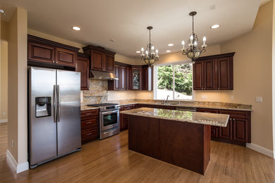 Photo of a mid-sized u-shaped eat-in kitchen in Seattle with an undermount sink, raised-panel cabinets, dark wood cabinets, granite benchtops, multi-coloured splashback, stone slab splashback, stainless steel appliances, light hardwood floors, with island, beige floor and yellow benchtop.