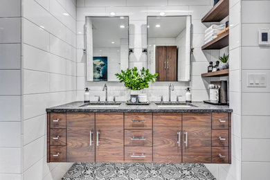 Inspiration for a medium sized modern ensuite bathroom in New York with flat-panel cabinets, medium wood cabinets, a freestanding bath, an alcove shower, a one-piece toilet, white tiles, metro tiles, white walls, porcelain flooring, a submerged sink, granite worktops, black floors, a sliding door, black worktops, a wall niche, double sinks and a floating vanity unit.