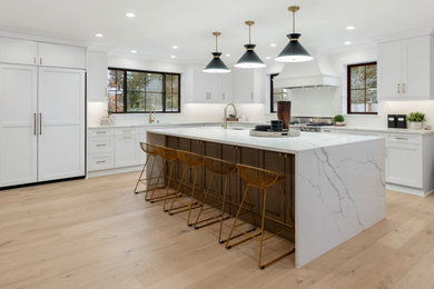 Example of a huge farmhouse l-shaped light wood floor and beige floor eat-in kitchen design in Seattle with an undermount sink, beaded inset cabinets, white cabinets, quartz countertops, white backsplash, ceramic backsplash, paneled appliances, an island and white countertops