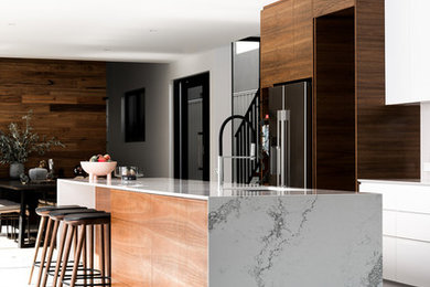 Inspiration for a large contemporary galley open plan kitchen in Perth with an undermount sink, flat-panel cabinets, white cabinets, quartz benchtops, white splashback, stone slab splashback, black appliances, concrete floors, with island and grey floor.