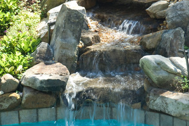 Photo of a large arts and crafts backyard custom-shaped natural pool in Other with a hot tub and natural stone pavers.