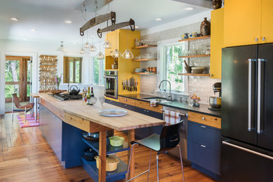 Eclectic galley medium tone wood floor eat-in kitchen photo in Providence with an undermount sink, flat-panel cabinets, yellow cabinets, white backsplash, subway tile backsplash, black appliances, an island and black countertops