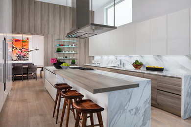 This is an example of a large modern galley separate kitchen in Miami with an undermount sink, flat-panel cabinets, white cabinets, marble benchtops, grey splashback, stone slab splashback, panelled appliances, light hardwood floors, with island, brown floor and multi-coloured benchtop.