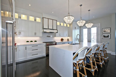 Large beach style l-shaped separate kitchen in Toronto with an undermount sink, shaker cabinets, white cabinets, marble benchtops, stainless steel appliances, dark hardwood floors, with island, brown floor and white benchtop.