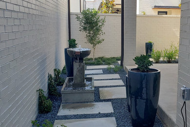 This is an example of a small modern side yard shaded xeriscape in Dallas with a water feature and concrete pavers.