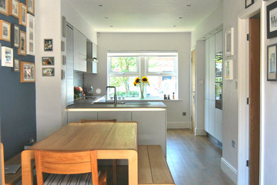 Photo of a medium sized contemporary kitchen/diner with flat-panel cabinets, grey cabinets, laminate countertops, grey splashback and a breakfast bar.