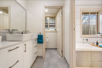 This is an example of a mid-sized master bathroom in Melbourne with white cabinets, a drop-in tub, a corner shower, a one-piece toilet, white tile, ceramic tile, ceramic floors, grey floor and a hinged shower door.