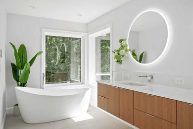 Diseño de cuarto de baño doble moderno con puertas de armario de madera oscura, bañera exenta, baldosas y/o azulejos blancos, paredes blancas, lavabo bajoencimera, suelo gris y encimeras blancas