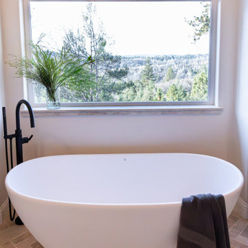 Freestanding tub beneath window with foothills view