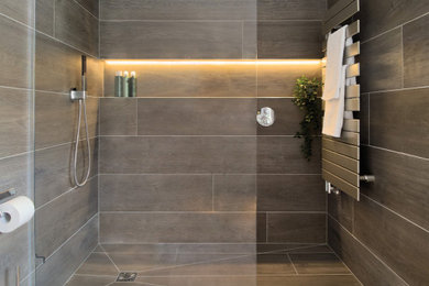 Large contemporary ensuite bathroom in Hampshire with glass-front cabinets, grey cabinets, a walk-in shower, a wall mounted toilet, brown tiles, porcelain tiles, porcelain flooring, a wall-mounted sink, glass worktops, an open shower, a single sink and a floating vanity unit.