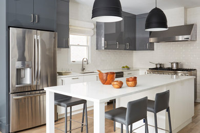 Kitchen - contemporary l-shaped medium tone wood floor and brown floor kitchen idea in Chicago with an undermount sink, flat-panel cabinets, gray cabinets, white backsplash, stainless steel appliances, an island and white countertops