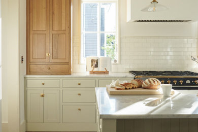 他の地域にある高級な広いトランジショナルスタイルのおしゃれなキッチン (エプロンフロントシンク、シェーカースタイル扉のキャビネット、グレーのキャビネット、白いキッチンパネル、サブウェイタイルのキッチンパネル、シルバーの調理設備、無垢フローリング、茶色い床、白いキッチンカウンター) の写真