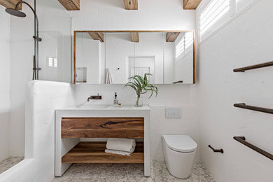 Large beach style bathroom in Sydney with open cabinets, medium wood cabinets, an open shower, a one-piece toilet, white tile, cement tile, white walls, pebble tile floors, an integrated sink, engineered quartz benchtops, beige floor, an open shower, white benchtops, a niche, a double vanity, a freestanding vanity and exposed beam.
