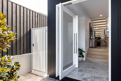 This is an example of a large modern foyer in Brisbane with black walls, travertine floors, a pivot front door, a glass front door and grey floor.